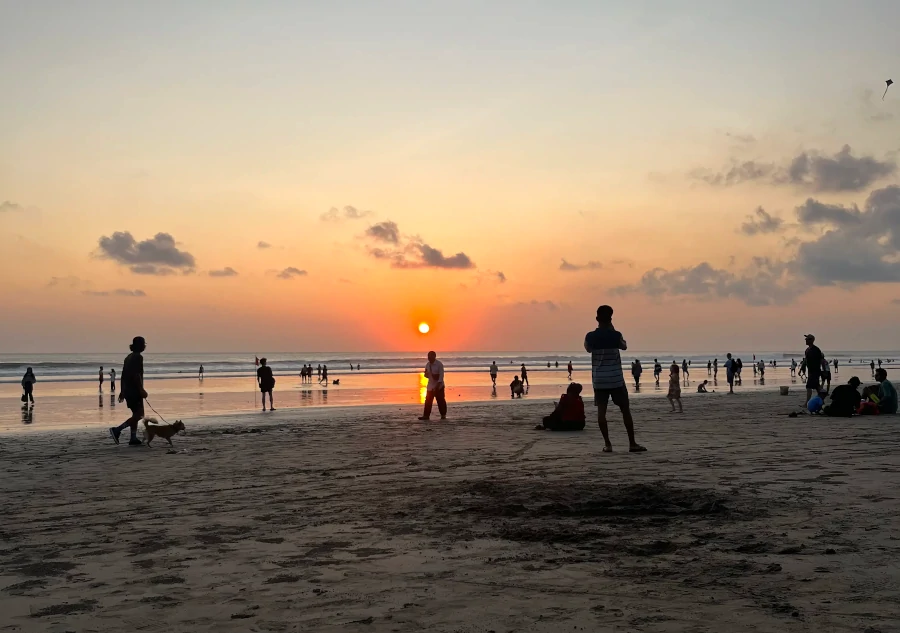 Atardecer en Kuta Beach con el sol poniéndose sobre el océano Índico y personas observando la puesta de sol desde la arena.