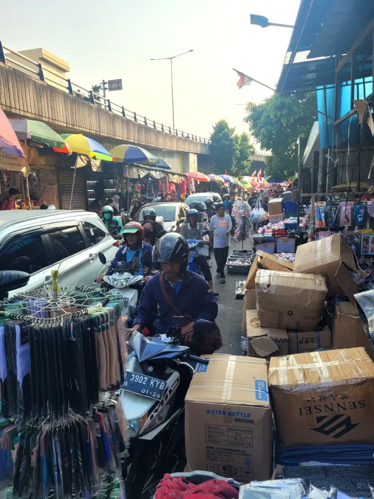 Street market del centro de Yakarta con motos, coches y puestos ocupando la calzada bajo un paso elevado