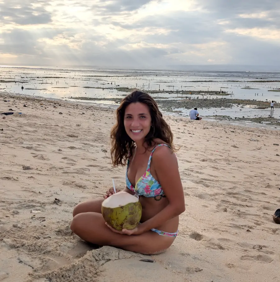 Viajera sentada en la arena de Mahagiri Beach, en Nusa Lembongan, disfrutando de un coco fresco junto al mar