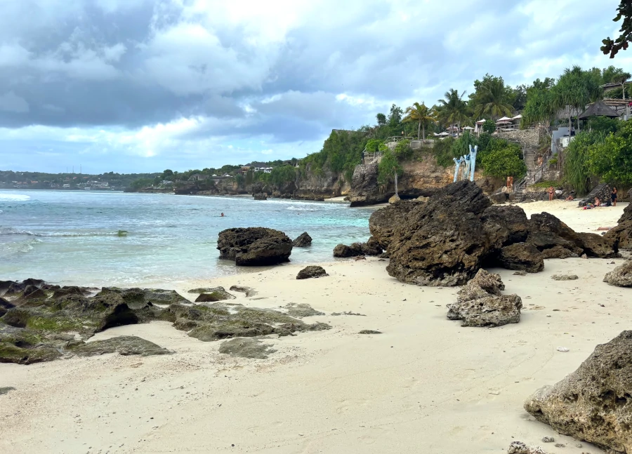 Playa de Nusa Ceningan con arena clara, rocas volcánicas y acantilados al fondo