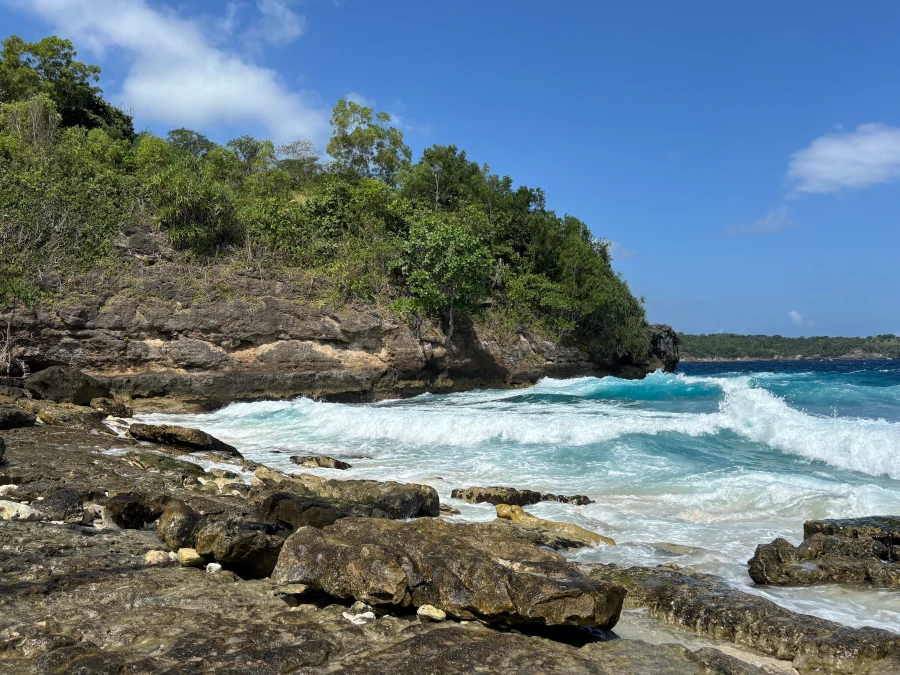 Costa rocosa de Nusa Ceningan con acantilados, vegetación tropical y olas rompiendo sobre el mar azul