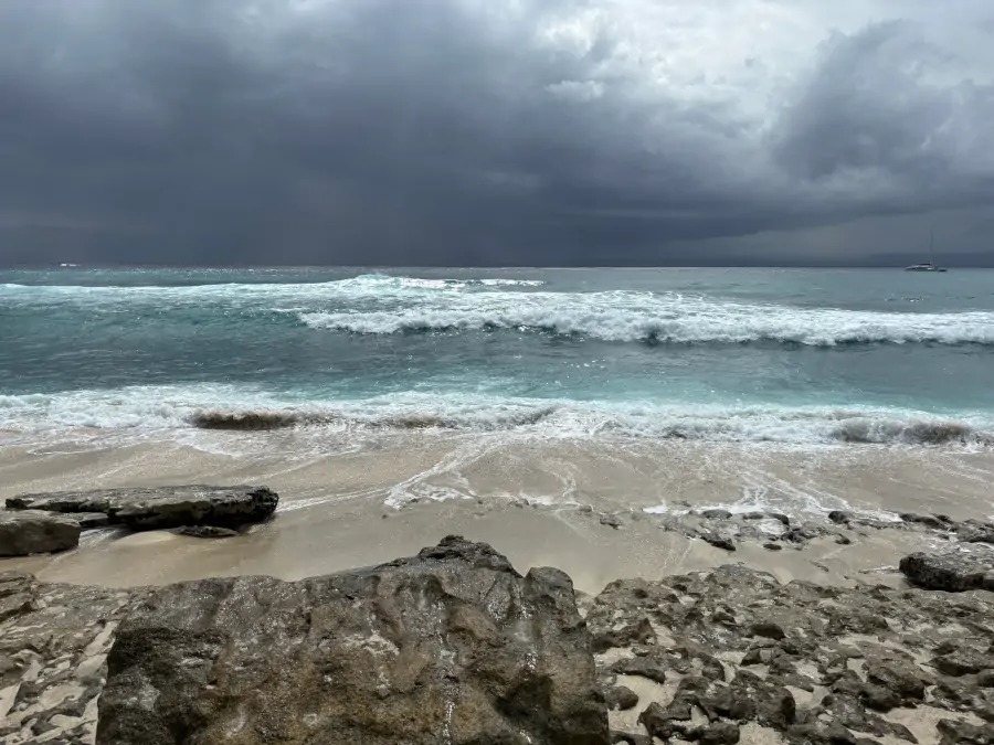 Olas rompiendo en Hidden Beach, en Nusa Lembongan, con rocas en la orilla y cielo nublado