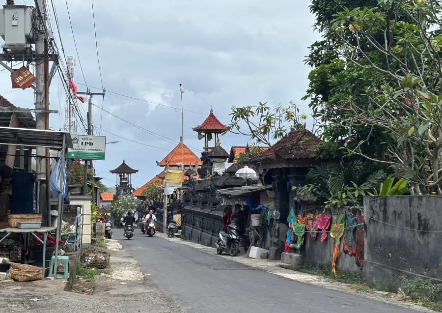 Calle de Nusa Lembongan con templos balineses, tiendas locales y motos circulando por el pueblo.