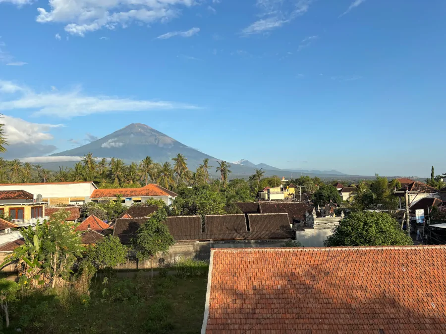 Vistas del monte Agung desde un alojamiento en Amed, Bali, con tejados, palmeras y el volcán al fondo
